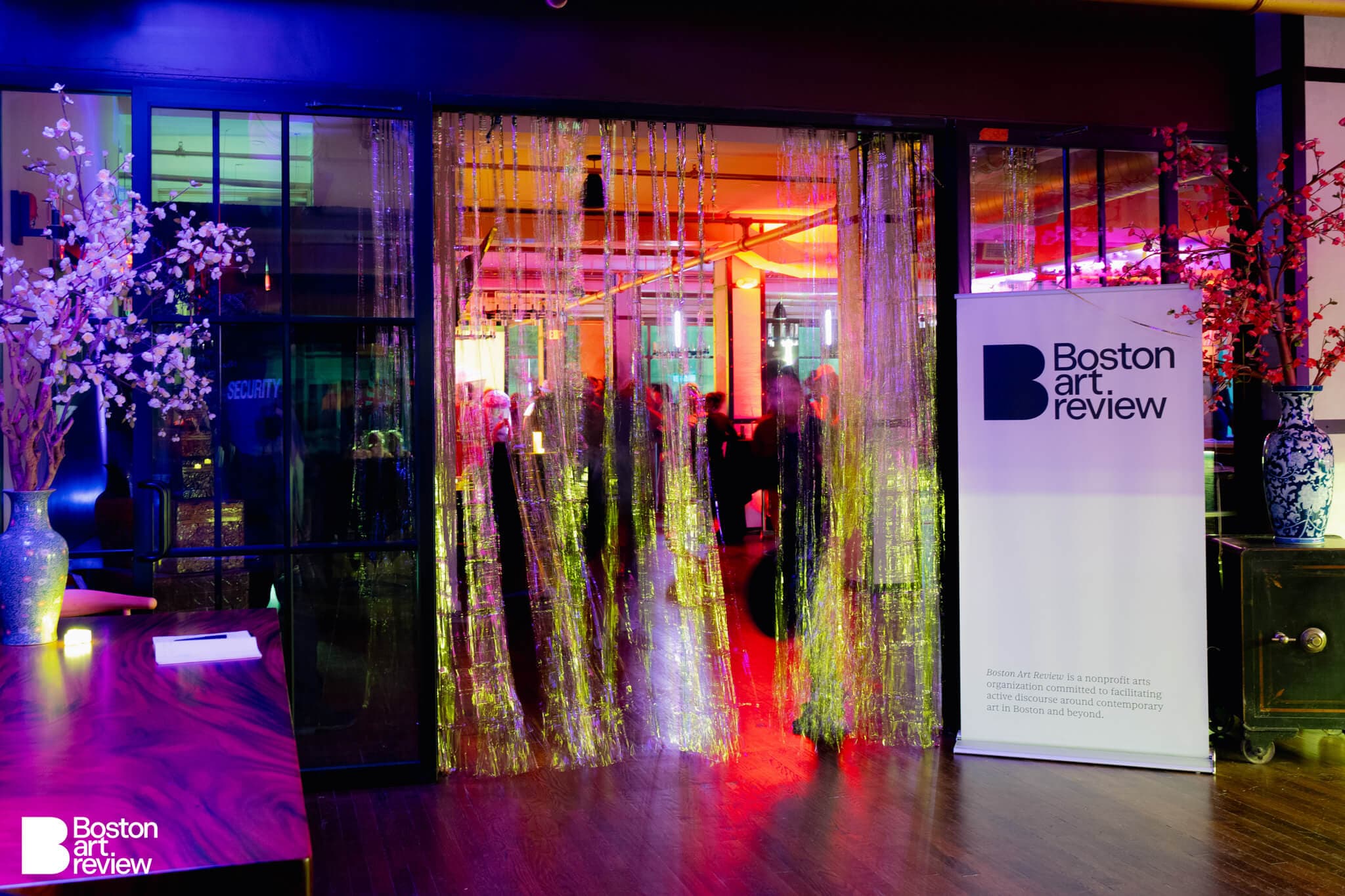 The entrance to the Boston Art Review Issue 13 launch party adorned with metallic streamers and backlit by an array of colorful lights.